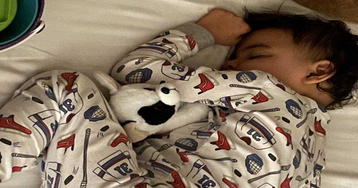 A young boy sleeps in hockey pyjamas with a stuffed dog inches arms.